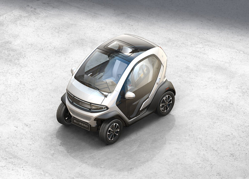 An overhead view of a compact, modern Eli ZERO micro EV with a transparent roof, parked on a textured gray surface.