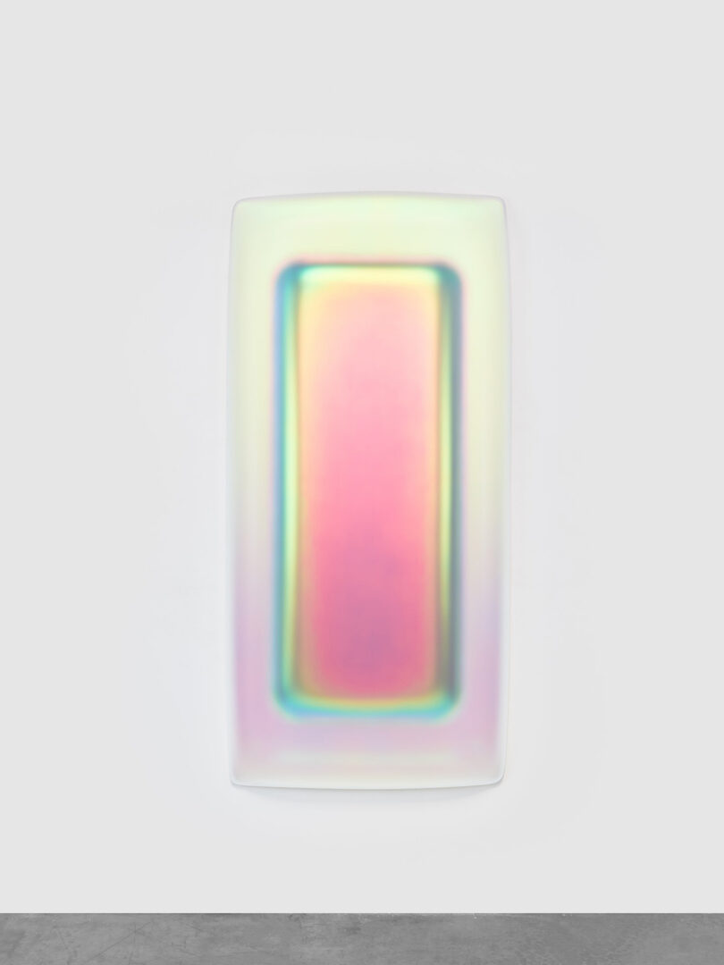 Abstract art on a white wall, displayed as a vertical rectangle with a blurred multicolor gradient from pink to green.