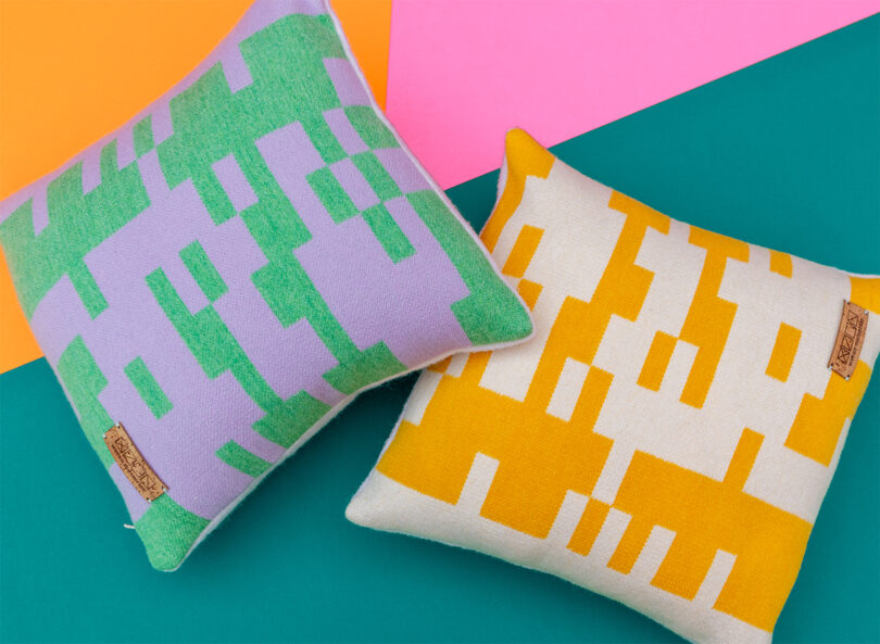 Two square pillows with pixelated designs on a multicolored background; one pillow is green and purple, and the other is yellow and white.