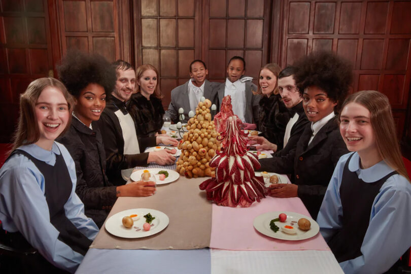 A diverse group of ten people with sitting at a dining table, smiling at the camera, with a decorative food centerpiece.