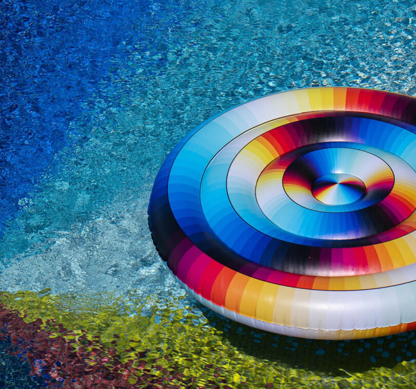 A vibrant, multicolored inflatable pool lounge designed by Felipe Pantone, resting on the surface of a clear blue swimming pool.