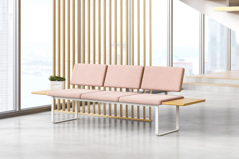 Modern pink upholstered modular bench with metal legs in a bright, spacious room with large windows and a city view.
