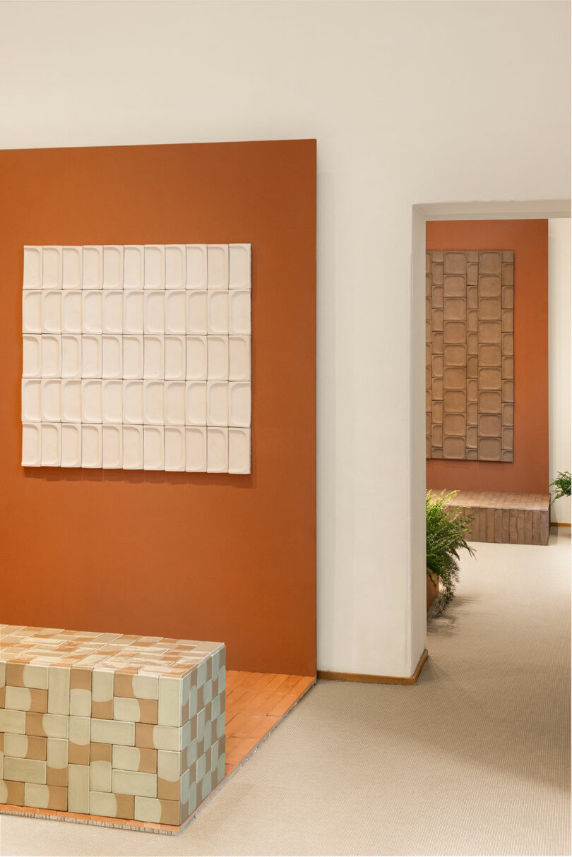 Art gallery interior with geometric wall art and matching checkered furniture. Walls painted in earthy tones, plants visible through an open doorway.