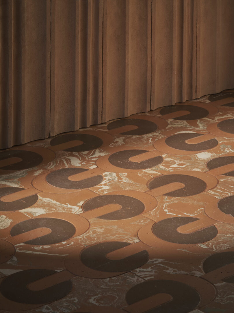 A floor with a curved brown and black patterned design next to a textured brown wall with vertical grooves.