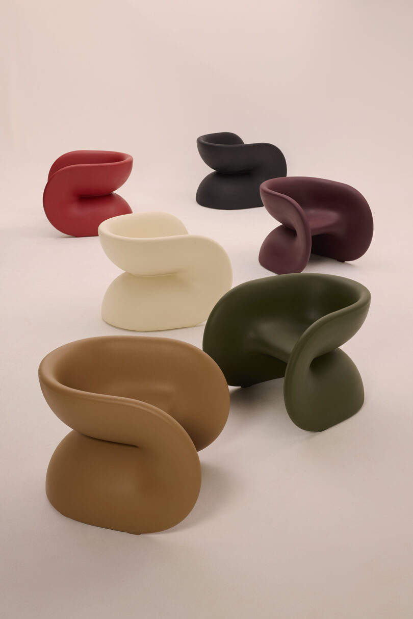 Six modern, curved chairs in various colors (red, black, maroon, cream, tan, and green) arranged on a plain background.