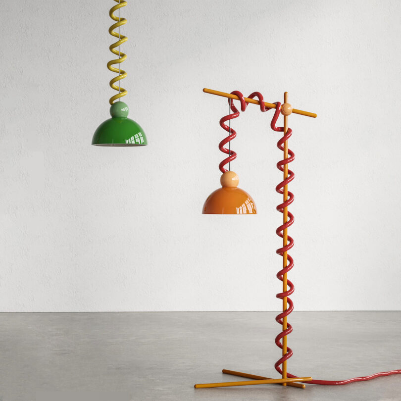 Two whimsical floor lamps with spiral red and yellow bases, and green and orange lampshades hanging in an empty room with a plain wall and floor