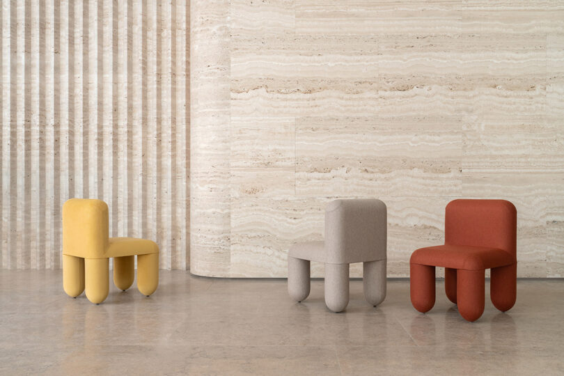 Three chairs in yellow, gray, and red placed against a textured beige wall in a modern interior setting.