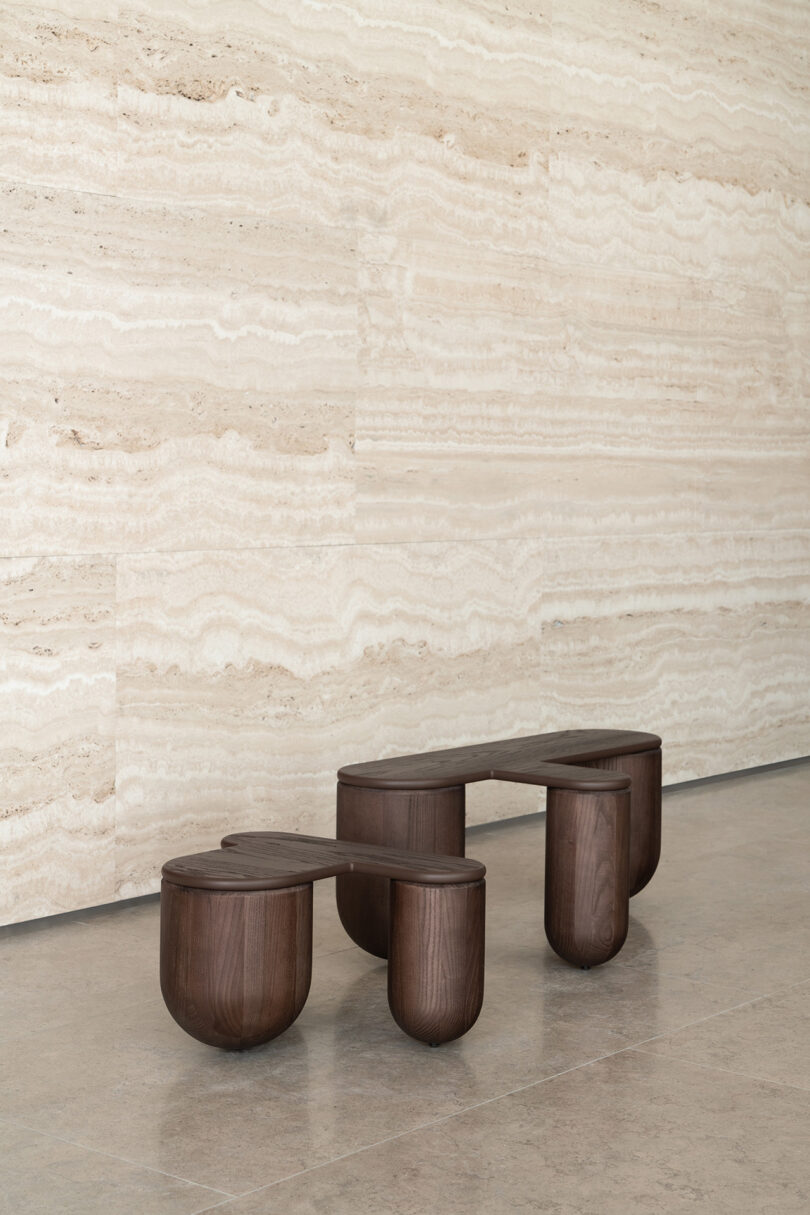 Two dark wood coffee tables against a striped stone wall in a minimalist indoor setting.