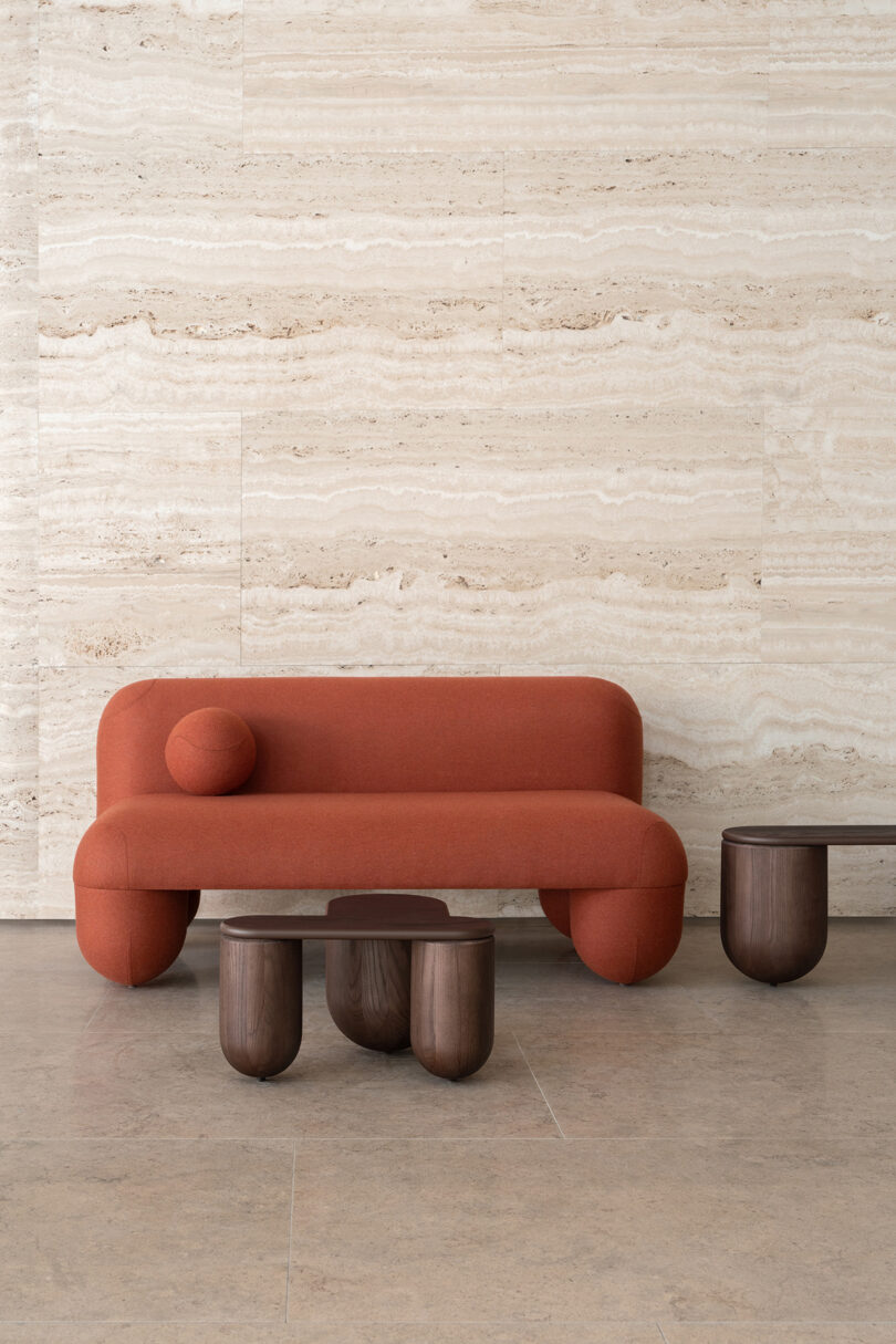 A modern red sofa with a curved design and two dark wood coffee tables positioned against a textured beige marble wall, with vertical stripe patterns to the side.