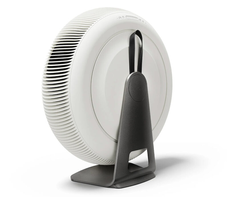 The IQ Air Atem X is a round, white air purifier with a vertical, gray stand on a flat surface, showcasing its back with a vented design.