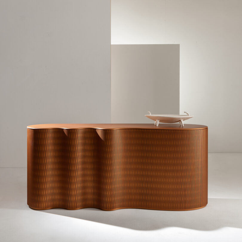 Curved wooden console in a minimalist room with a white backdrop and a small tray on top