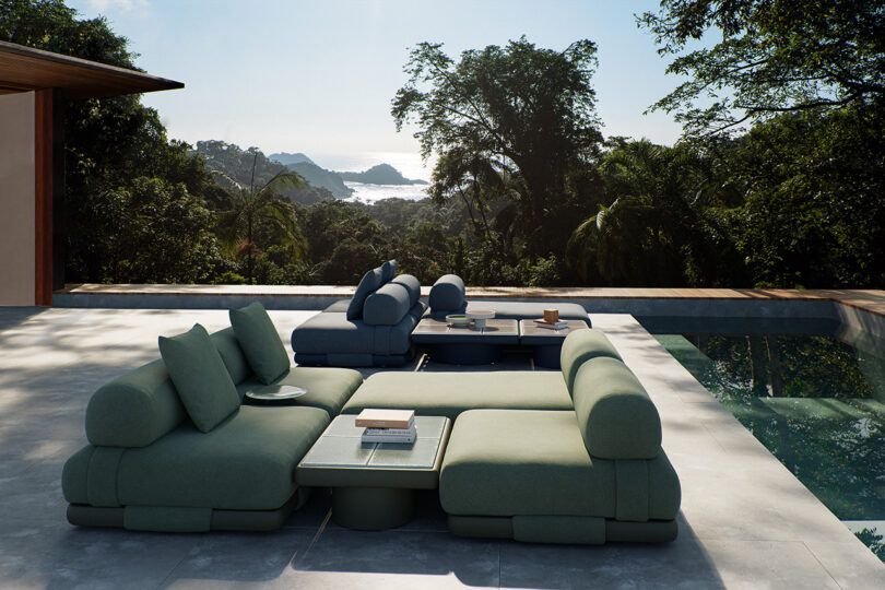 Outdoor seating area with green and blue modular sofas near a pool, set against a backdrop of lush greenery.