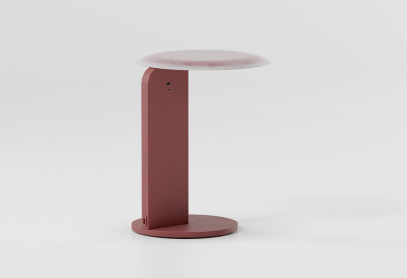 A modern, minimalist red table with a round base and a flat, circular tabletop.