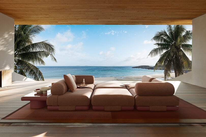 Outdoor space with a large pink modular sofa, side tables, and a view of a beach, ocean, and palm trees.
