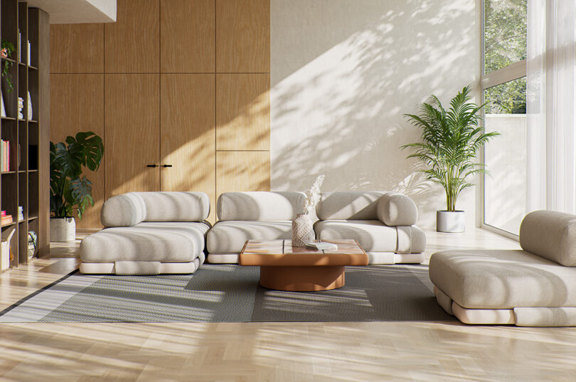 A contemporary living room with light-colored modular sofas, a coffee table, large floor-to-ceiling windows, indoor plants, wooden panel walls, and a bookshelf on the left.
