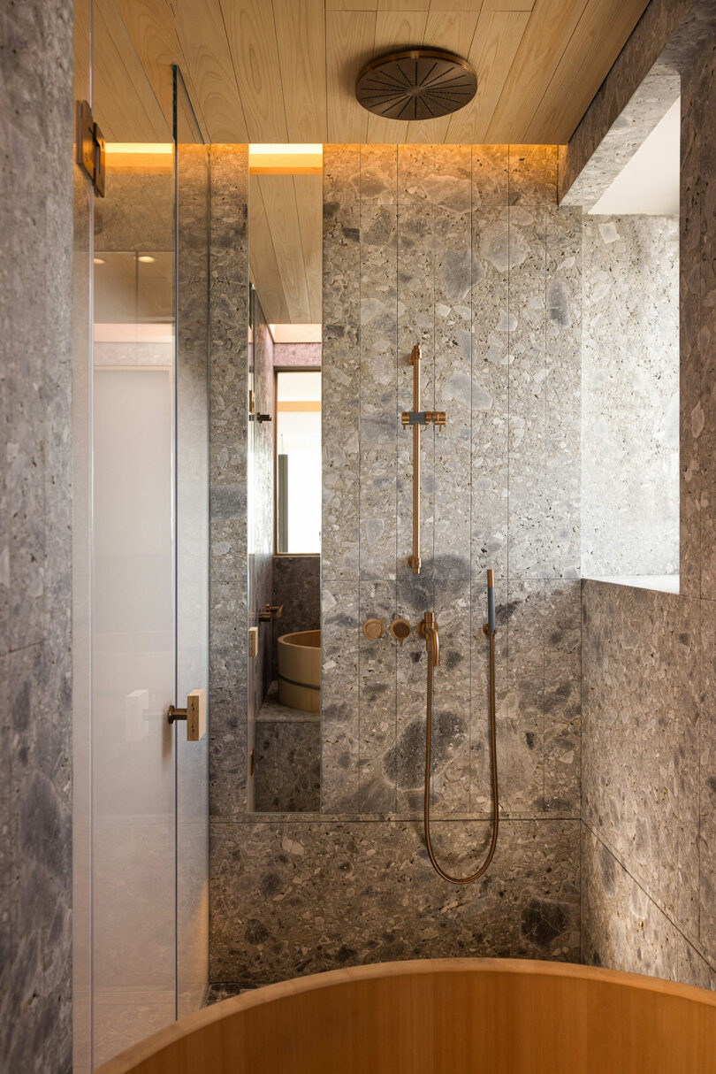 Modern bathroom featuring marble walls, a glass shower door, and wood-paneled ceiling with a mounted showerhead.