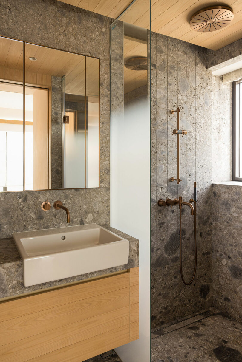 Angled view of modern bathroom with textured stone walls and wood floating sink