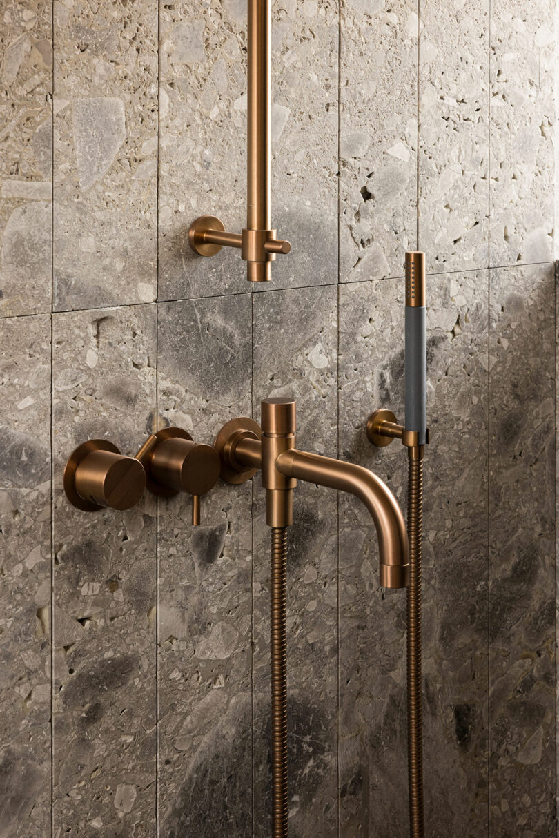 Modern copper shower fixtures mounted on a textured stone tile wall.