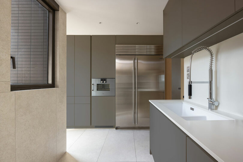 Modern kitchen interior with taupe cabinets, a built-in refrigerator, and a large white island with a sink.