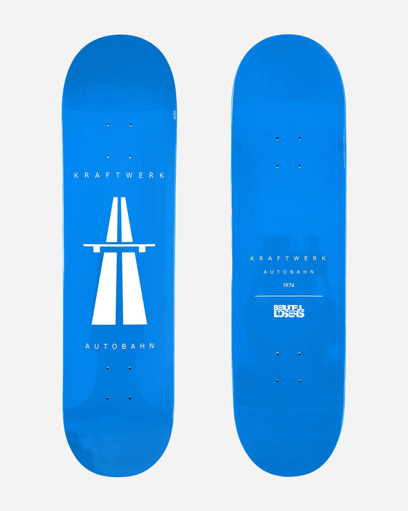 Two blue skateboards with white text and graphics are part of the Kraftwerk Collection Skateboard Decks. One features a highway symbol and the words "Kraftwerk Autobahn." The other has small text reading "Kraftwerk Autobahn 1974" and "Blufff Lovers.