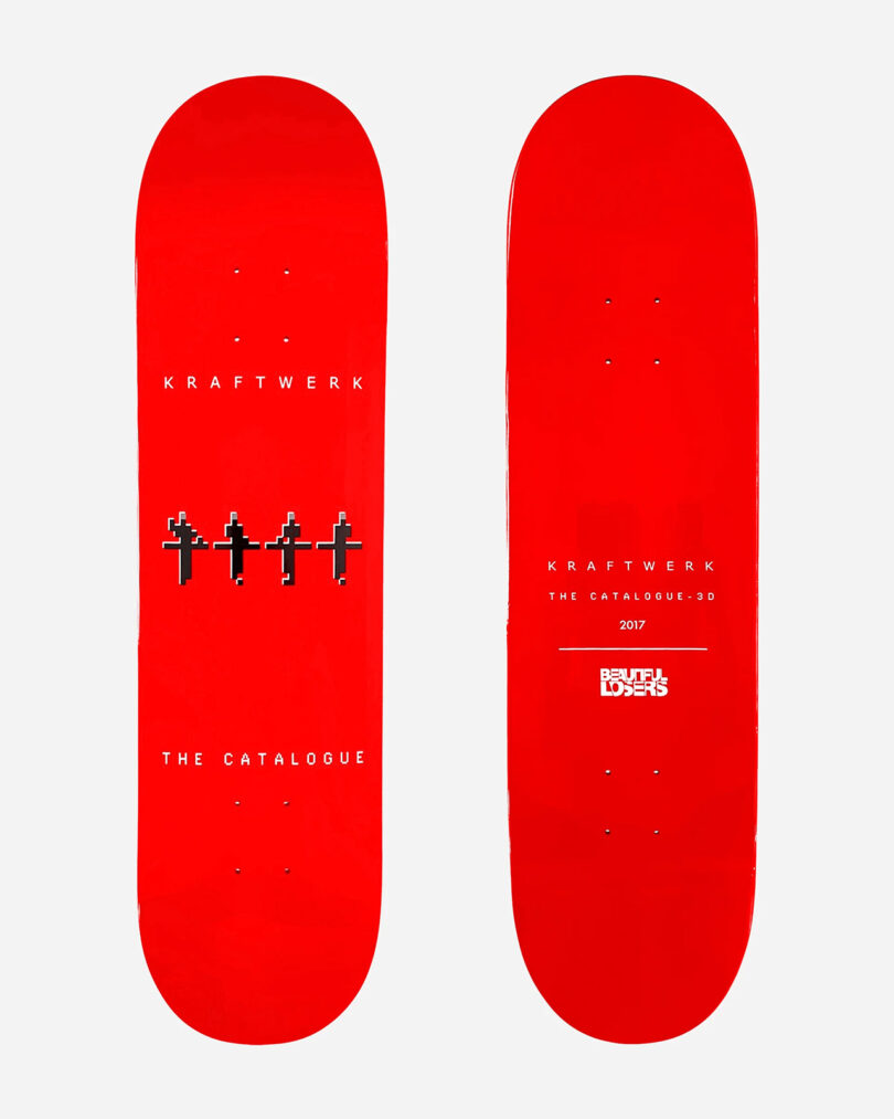 Two red skateboards from the Kraftwerk Collection Skateboard Decks are displayed side by side. The left one features pixelated figures and the text “Kraftwerk: The Catalogue.” The right one has text “Kraftwerk,” “The Catalogue 3D,” and “2017 Skate Dolls.”