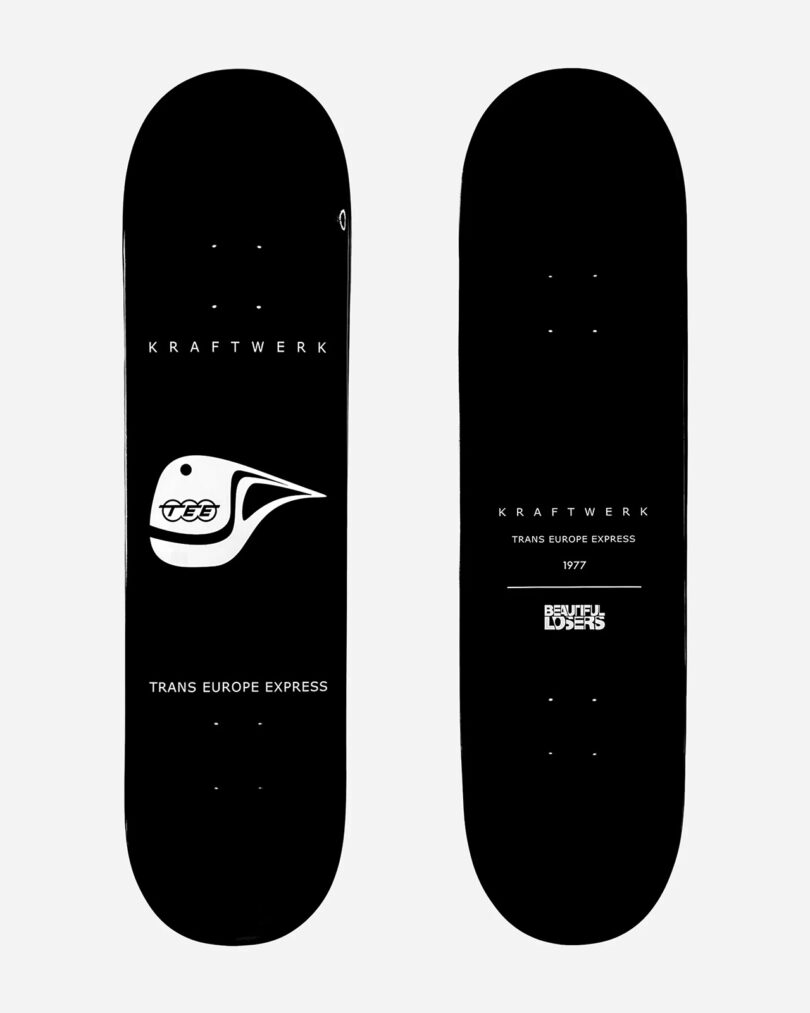 Two black skateboards are displayed, part of the Kraftwerk Collection Skateboard Decks. Both feature white graphics: one has a helmeted face with "Kraftwerk" and "Trans Europe Express" text, while the other includes "Kraftwerk," "Trans Europe Express," and "Deutsche Autobahn" text.