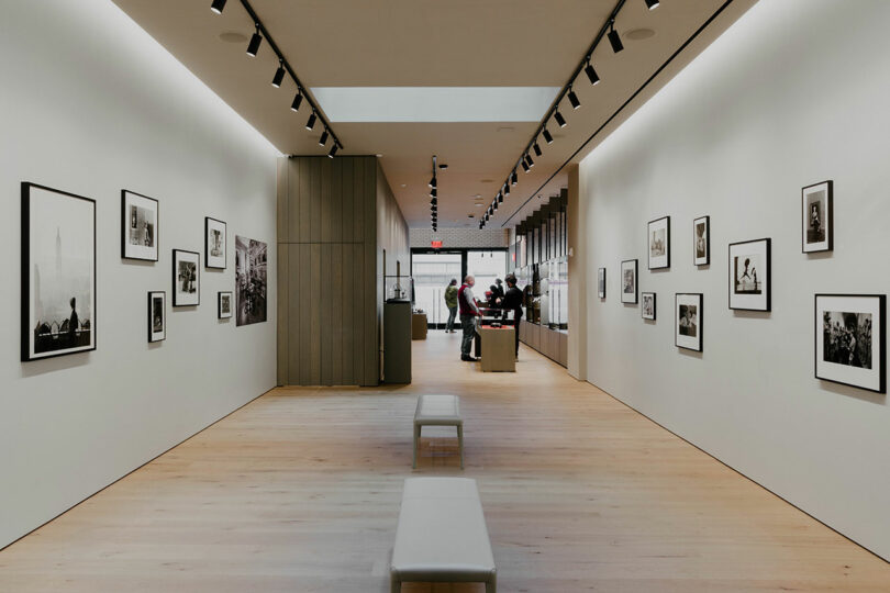 Interior of a modern art gallery displaying black and white photographs on the walls, with visitors viewing the artwork in the distance.