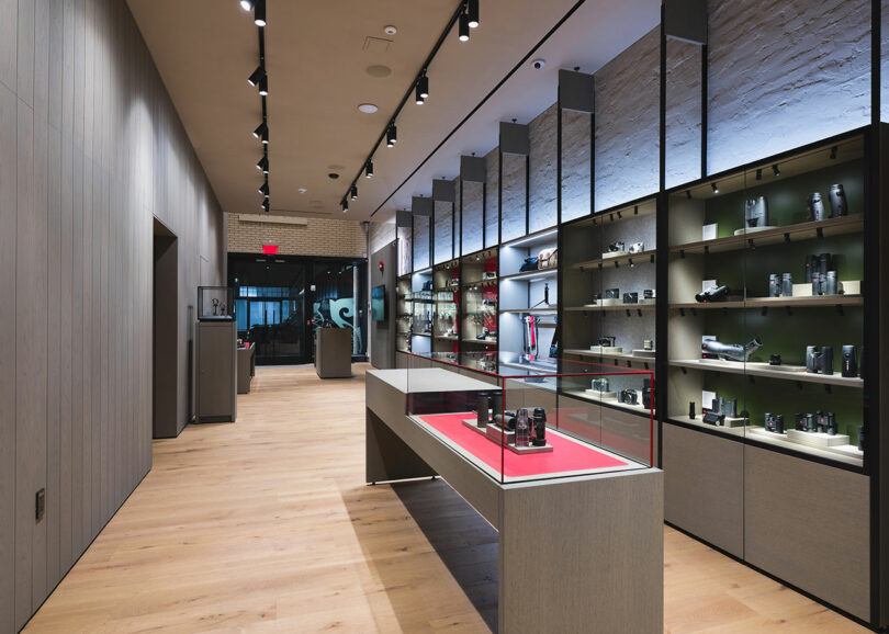 Modern retail store interior featuring sleek shelving with a variety of products, wooden floors, dim overhead lighting, and reflective surfaces.