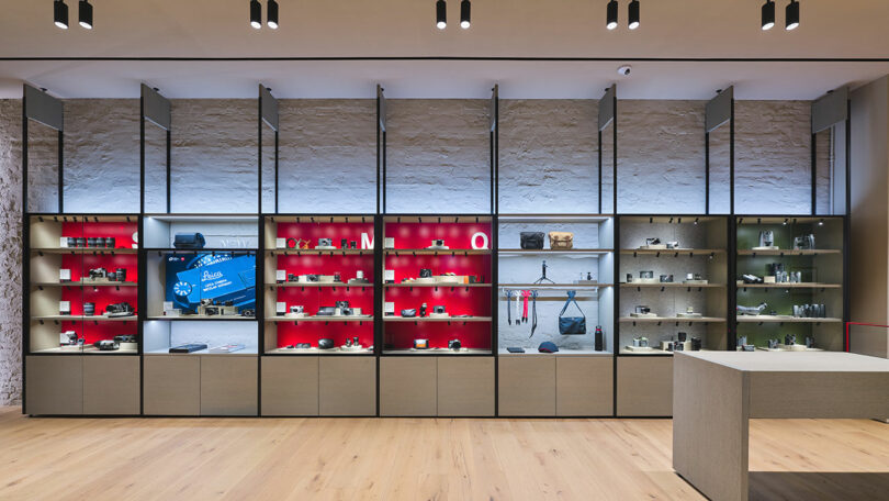 Interior of a modern store showcasing electronics with products displayed on red and grey shelves, wooden flooring, and white walls.