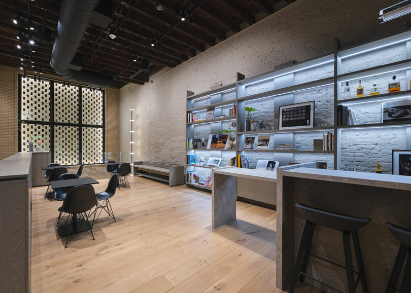 Modern café interior with bar stools, tables, and shelves stocked with books and products, featuring exposed brick and wooden floors.