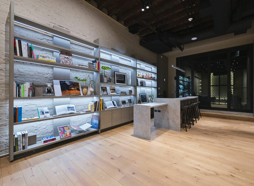 Modern bookstore interior with shelving units displaying books and magazines, a coffee bar with stools, and exposed brick and wooden beams.