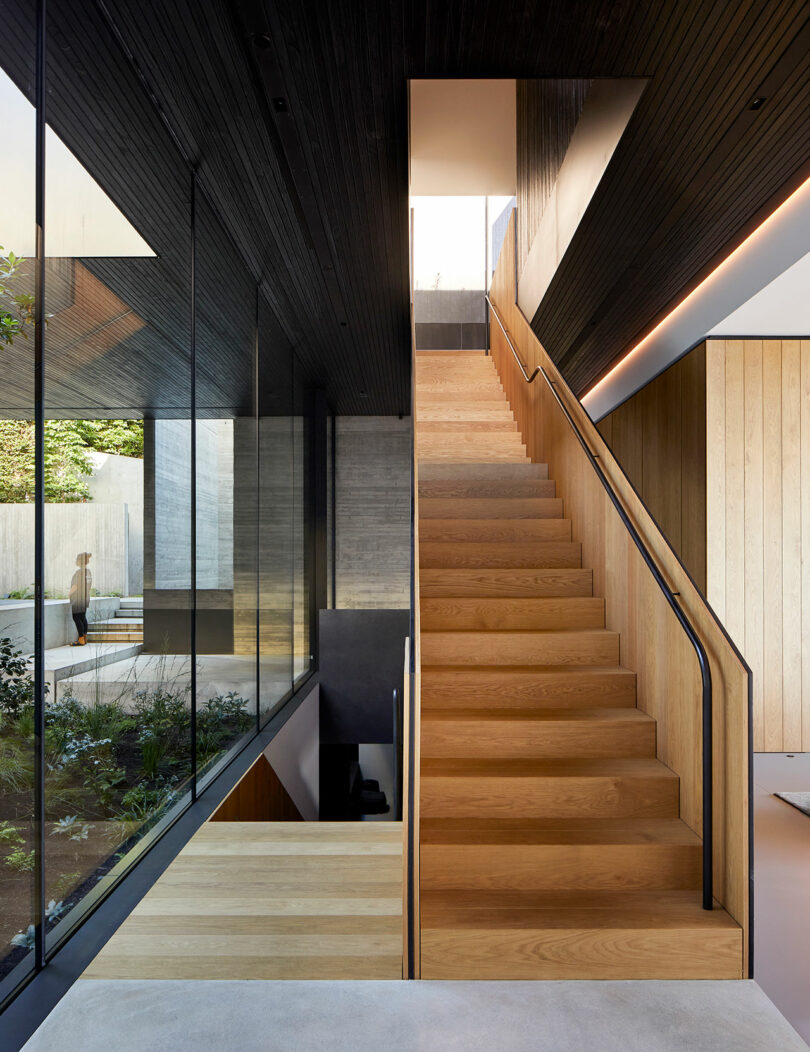 View of modern wood staircase next to wall of windows in a modern house.