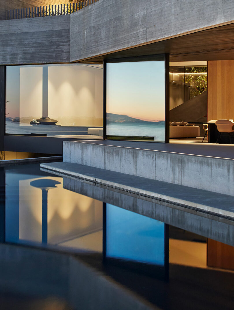Liminal house with large windows showing a sunset over the ocean, reflected in a sleek infinity pool.