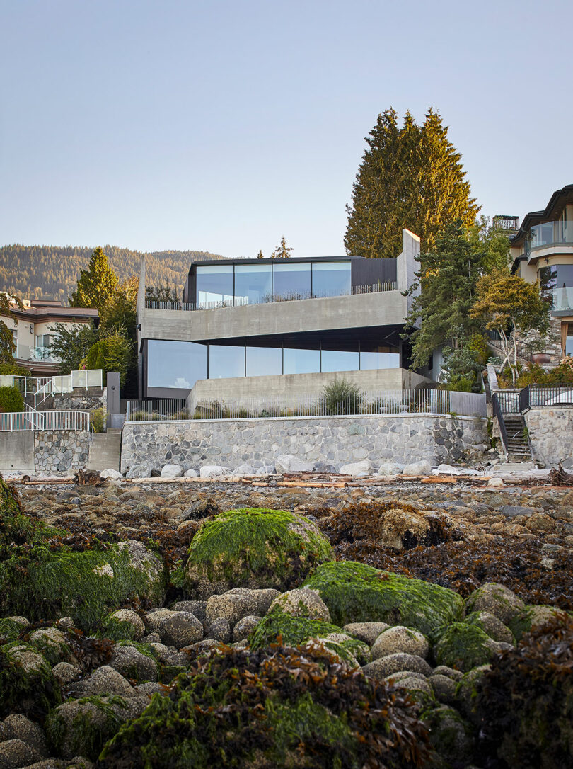 View of backside of modern concrete house with angular design looking up from a rocky cliff.