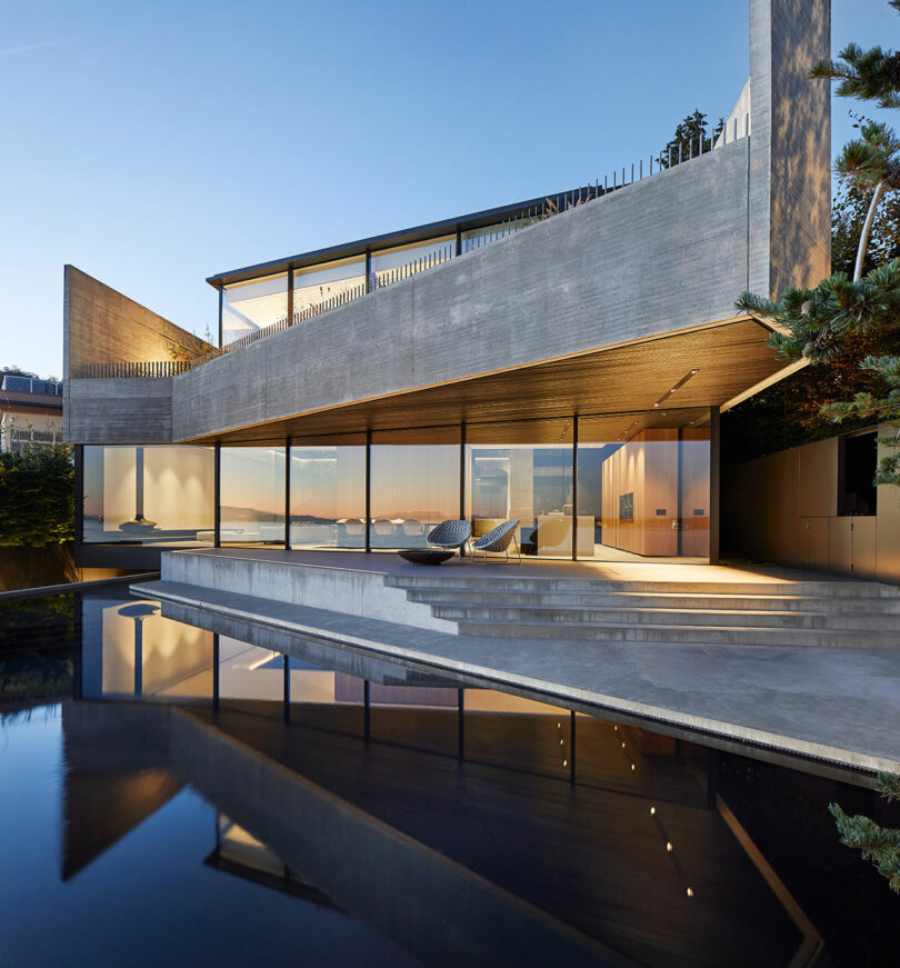 Liminal house with large glass windows, reflecting pool in the foreground, and a sunset view in the background.