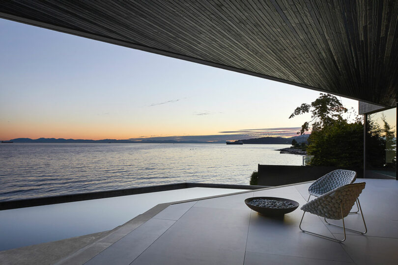 Modern patio with stylish chairs overlooking a serene ocean sunset, under a textured overhang at the Liminal House.