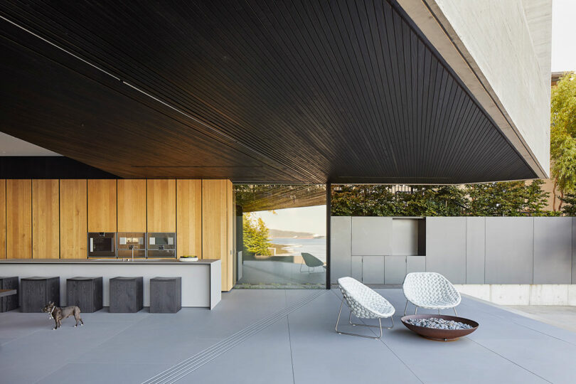 Modern outdoor patio with wooden paneling, sleek kitchenette, minimalist furniture, and a view of the hillside at the Liminal House.
