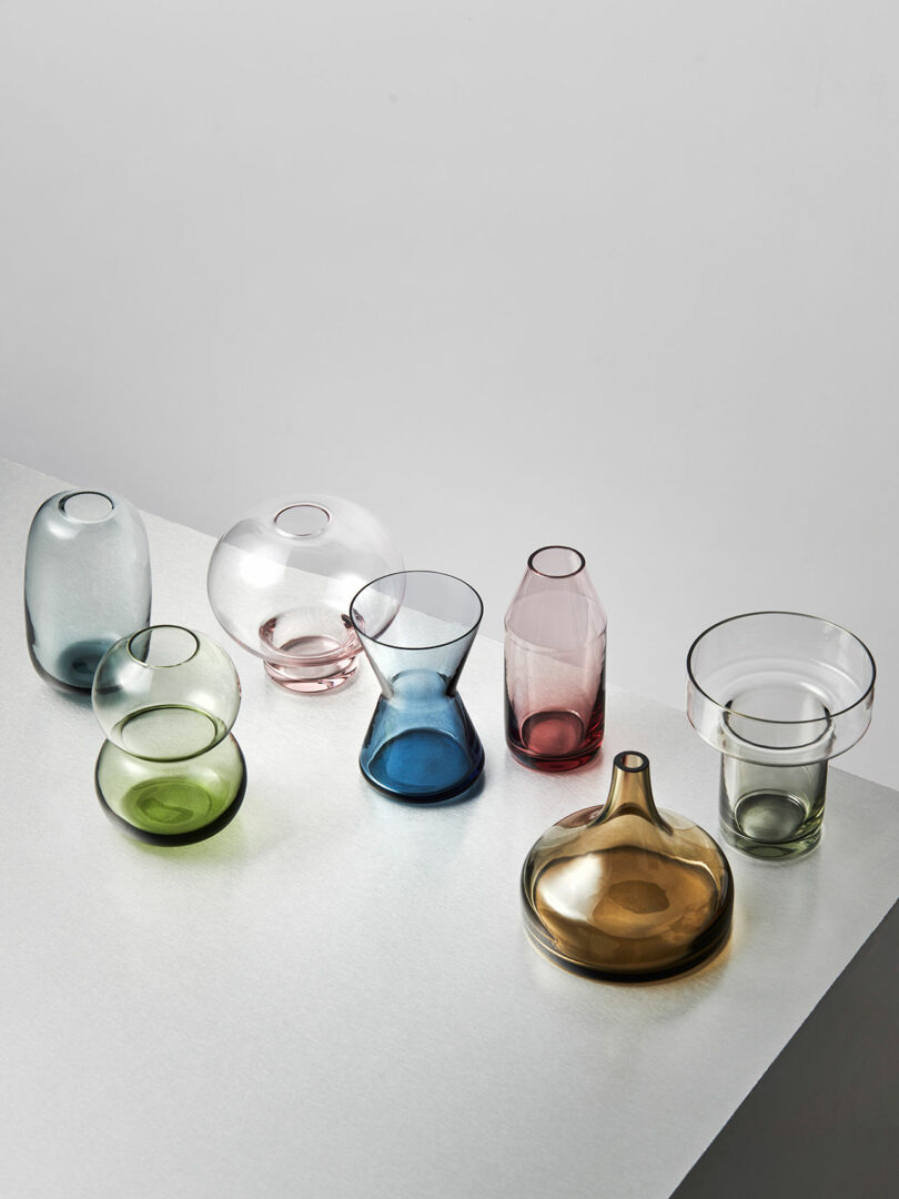A variety of colorful glass vases and containers of different shapes and sizes are arranged on a light surface.