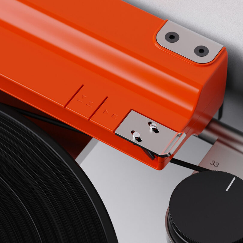 Close-up of a vibrant orange Disco Volante Turntable tonearm and stylus on a vinyl record, highlighting intricate features and texture, with dial to the right.