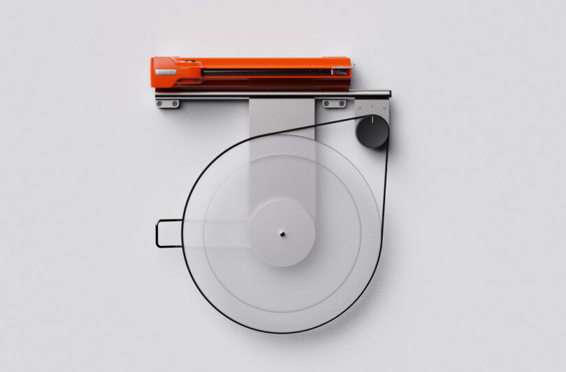 A minimalist Disco Volante Turntable with a transparent platter and an orange arm against a plain white background.