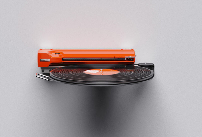 A vibrant orange Disco Volante Turntable with a spinning vinyl record, set against a plain gray background.