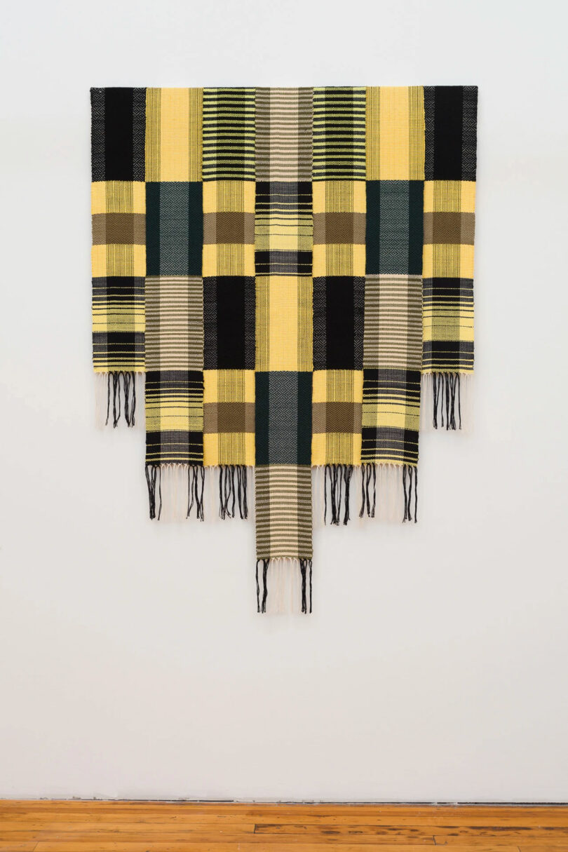 Yellow and black woven textile art hanging on gallery wall