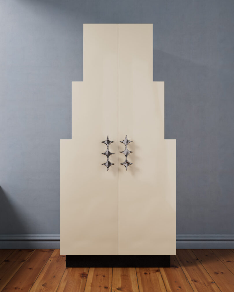 A uniquely stepped cabinet with geometric silver handles stands on a wooden floor against a gray wall.