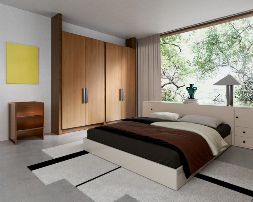 A modern bedroom with a large window, wooden wardrobe, and a low platform bed with brown and white bedding. A small wooden dresser stands near a yellow wall art piece.