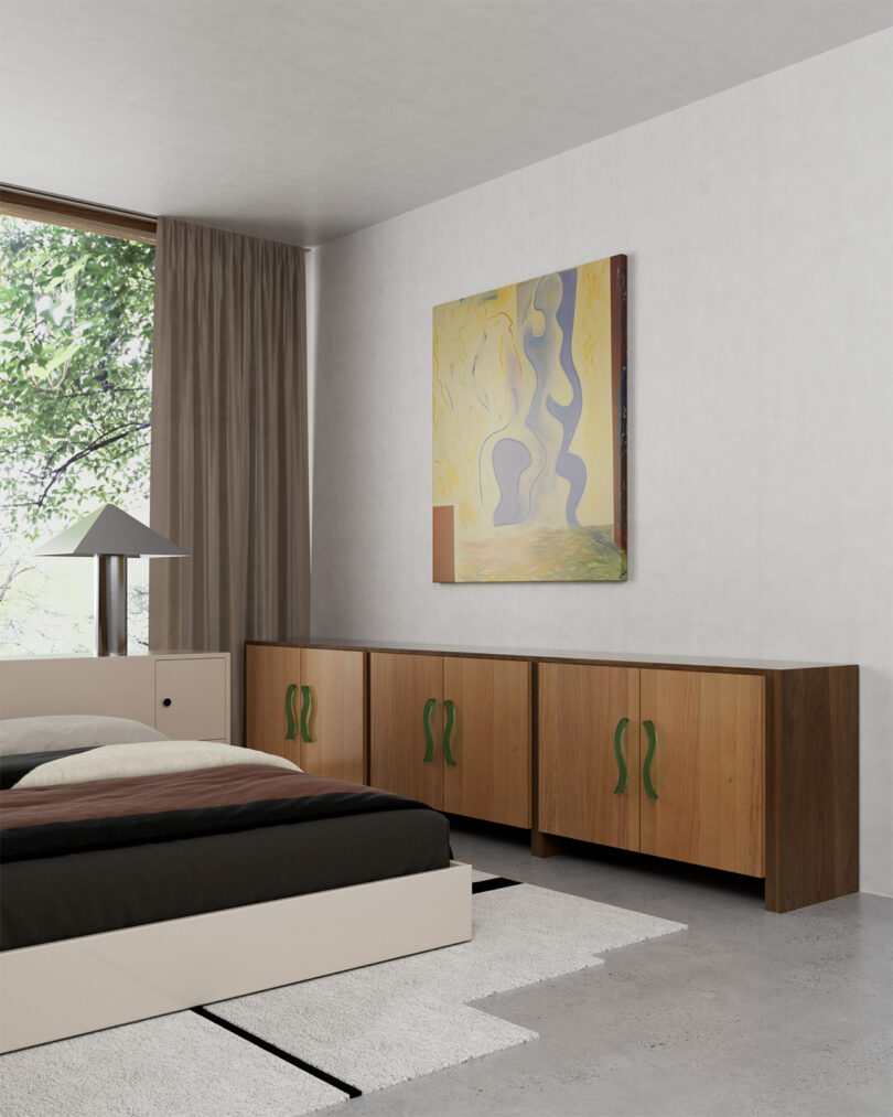 A modern bedroom with a large window, a bed with a brown and white color scheme, a wooden sideboard with green handles, light-colored walls, and a contemporary abstract painting hanging above the sideboard.