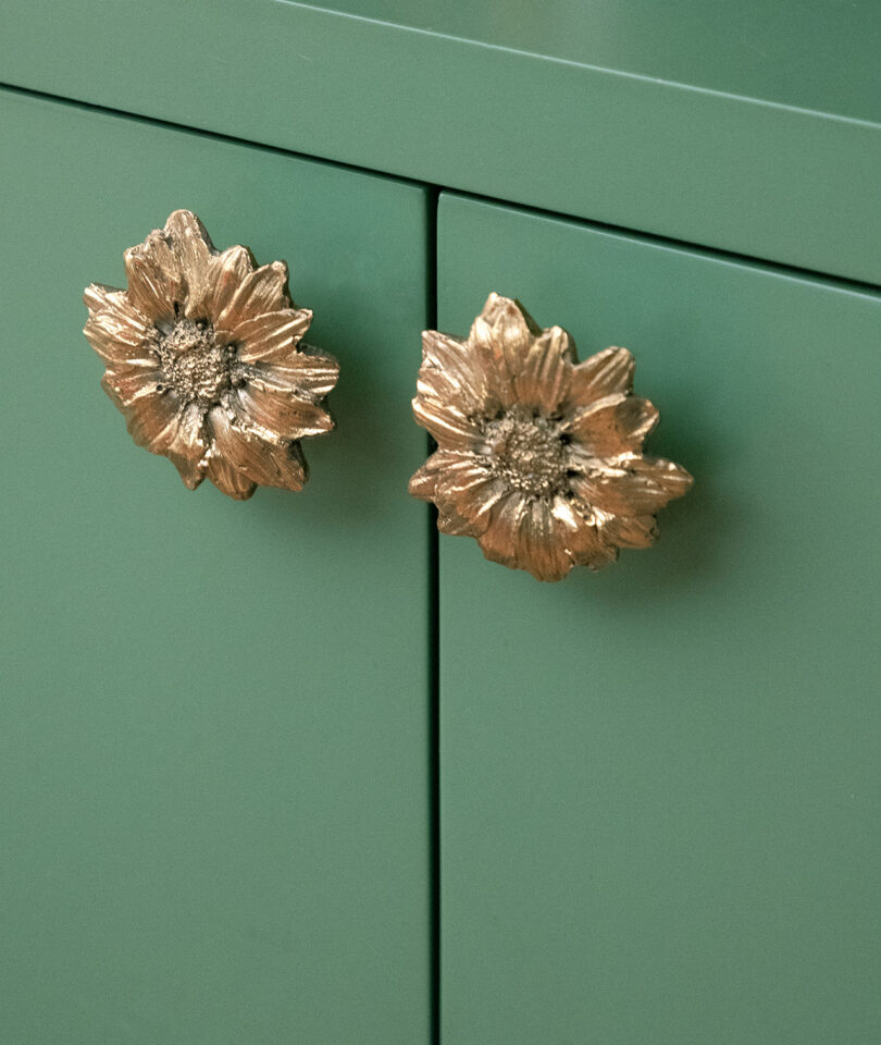 Close-up of two green cabinet doors with gold flower-shaped handles.