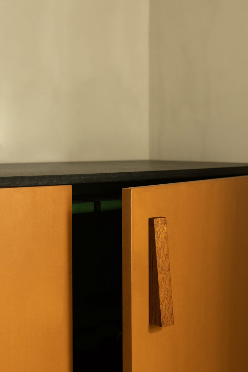 A wooden cabinet with a black countertop and one door slightly ajar, featuring a matching wooden door handle.