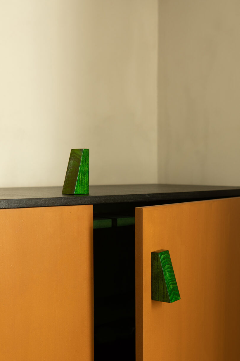 Two wooden cabinet doors with green triangular handles partially open.