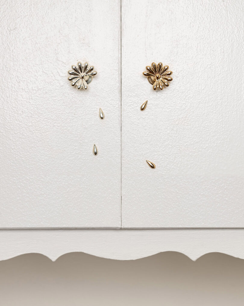 Two cabinet doors with floral-shaped knobs and petal-shaped embellishments hanging below each knob, set against a white background.