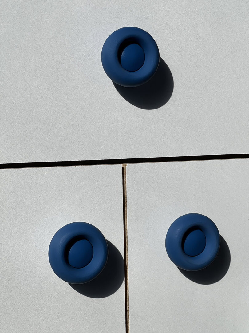 Three blue circular knobs on a white cabinet.